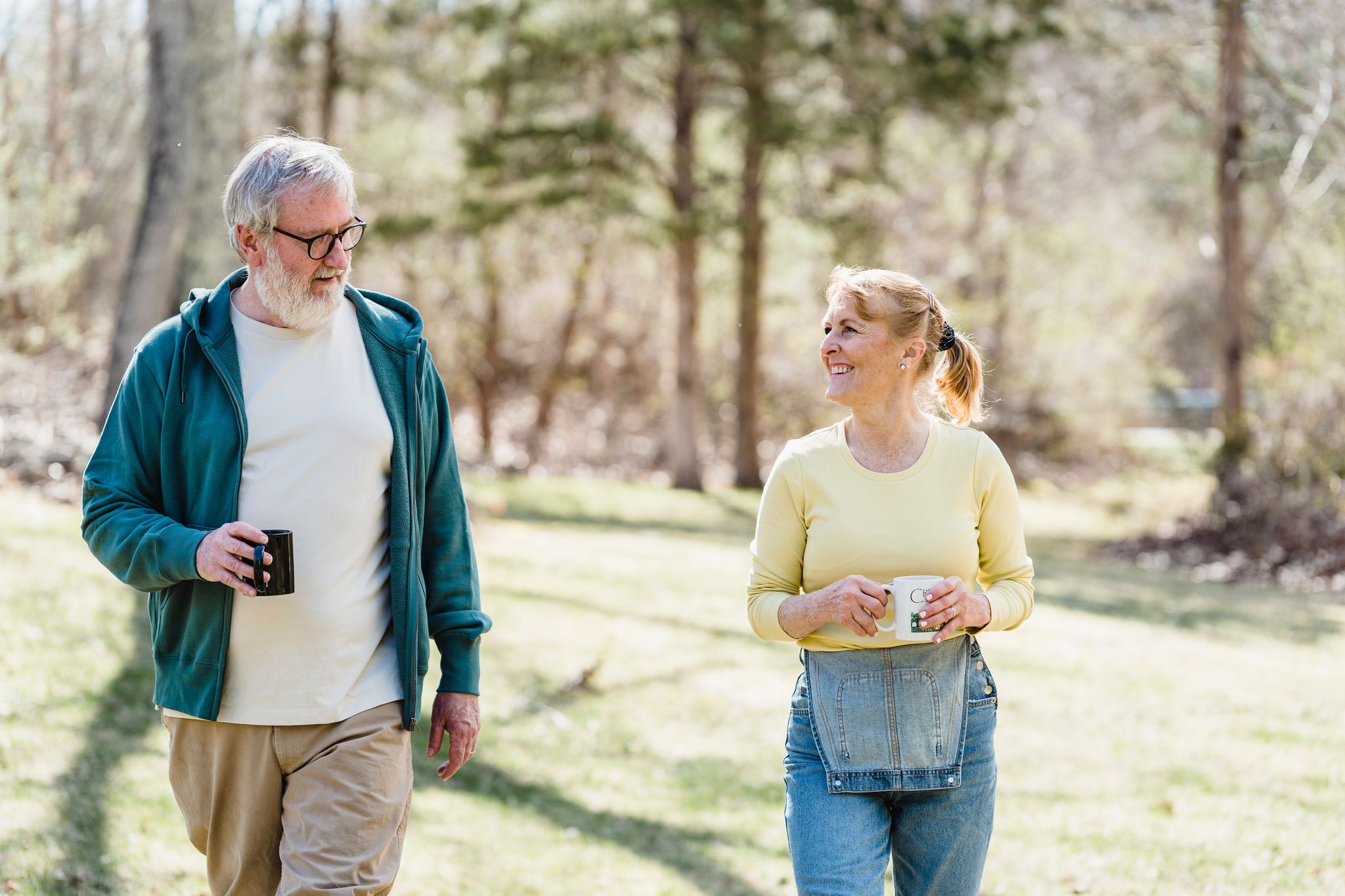 senior couple walking outdoors together both holding coffee cups and looking at each other