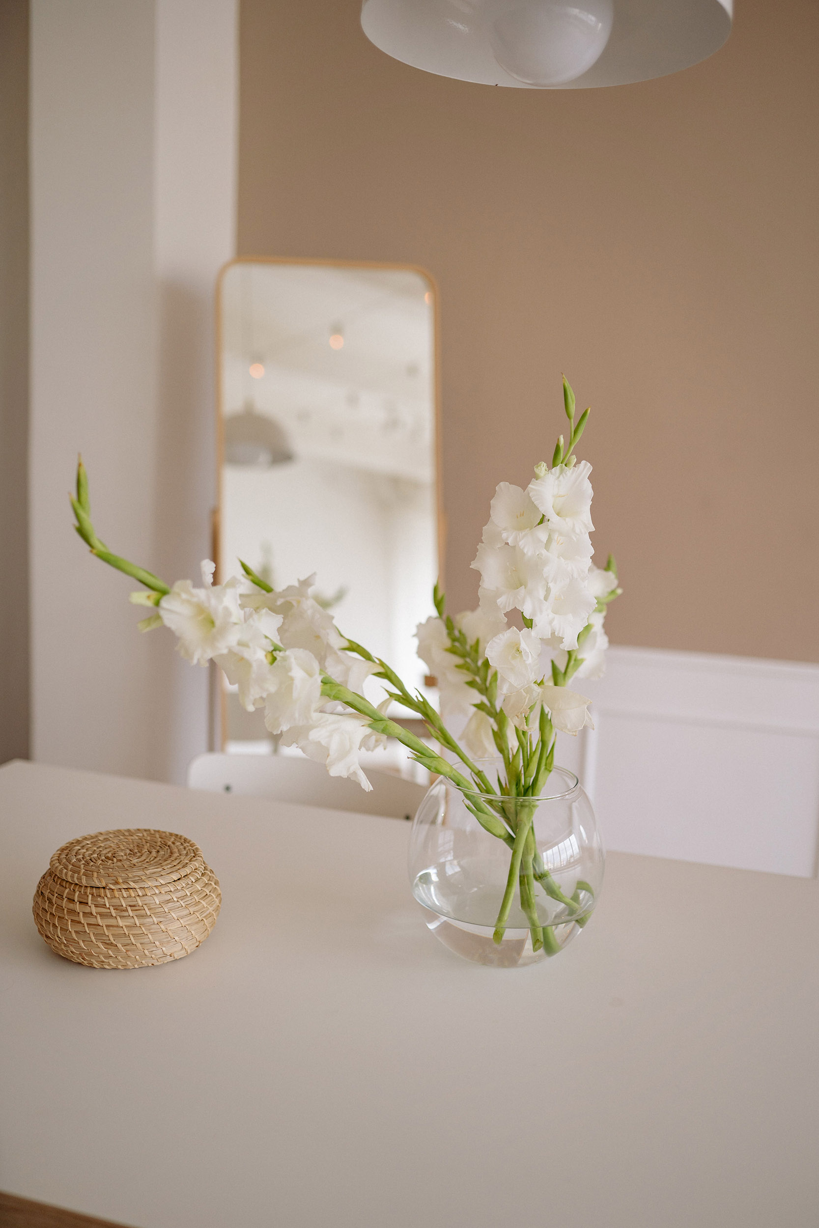 A vase with white flowers and a mirror in the back on a table